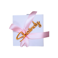 White personalized gift box wrapped with a pink satin ribbon and gold “Chanu...ly” name decoration.