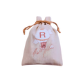 Personalized beige drawstring gift pouch featuring a teddy bear illustration, floral details, and a red monogram letter.