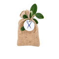 Small beige burlap drawstring favor pouch decorated with green leaves and a white personalized tag featuring a blue scissors symbol.