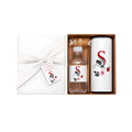 Elegant personalized gift set featuring a white wrapped box with a floral gift tag, a matching bottle of treats, and a tall white bottle with a red monogram and floral design.