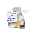 Small white mesh gift pouch tied with a black-and-white ribbon, containing a yellow sponge and featuring a blue handwritten gift tag.